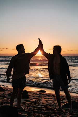 zwei Freunde machen high five am Stand bei Sonnenuntergang